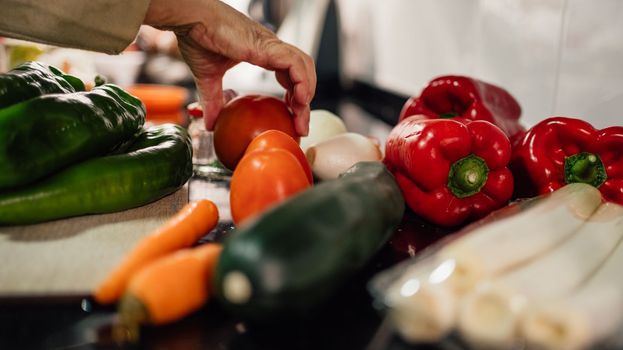 A female chef holding and picking a fresh tomato from vegetables on the table.