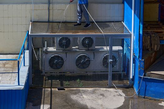 a substance or appliance used to improve or maintain something's condition. A worker washes cleans the air conditioning system in the backyard of a factory.