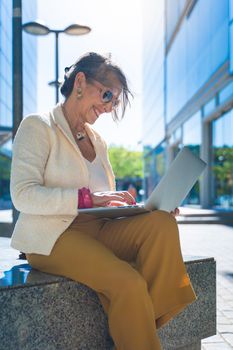 Happy attractive business woman middle-aged working smiling with laptop in front of a modern building. Vertical photo. High quality photo