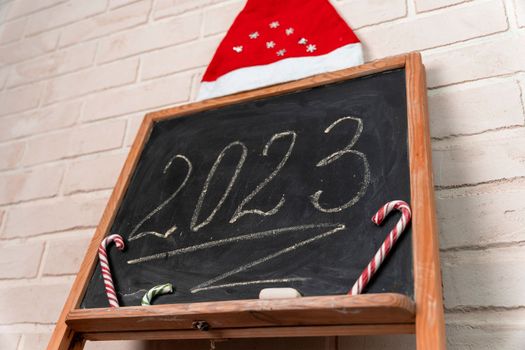 a black slate decorated with candy in the form of a caramel cane. The year 2023 is written in chalk on the blackboard. Happy New Year. 2023. Number written in chalk on a school board