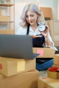 Starting small business entrepreneur of independent Asian woman smiling using computer laptop with cheerful success of online marketing package box items and SME delivery concept.