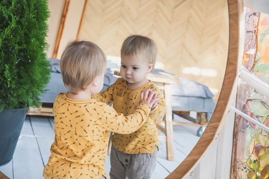 beautiful blonde baby in the bedroom near the mirror and looks at his own reflection