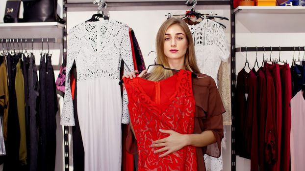 Sexy girl, tall, beautiful blond woman chooses clothes in the store, admiring herself in front of a mirror, smiles. Shopping in a stylish clothing store. slow motion. High quality photo