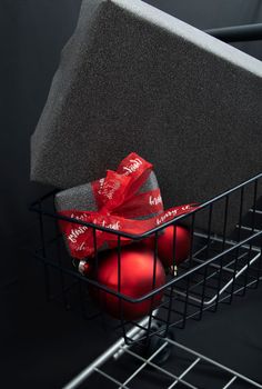 Christmas gift boxes in black paper in a shopping basket with red balls on a black background. High quality photo