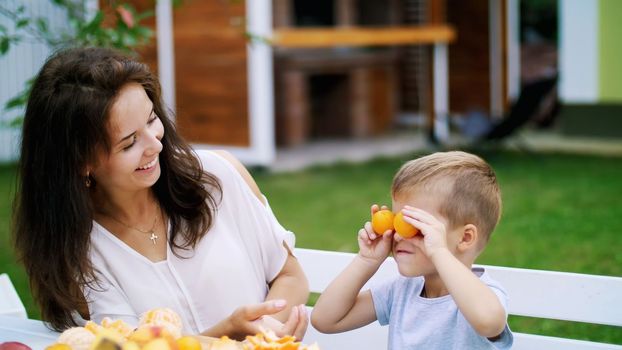 summer, in the garden. a four-year-old boy, having fun with his family outdoors, twisting, applying mandarins to his eyes. family holidays, lunch on the nature, in the courtyard. High quality photo