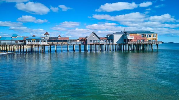 Image of Aerial side profile of long old wood pier covered in shops in Maine with ocean and blue sky