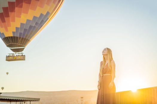 Tourist woman looking at hot air balloons in Cappadocia, Turkey. Happy Travel in Turkey concept. Woman on a mountain top enjoying wonderful view.