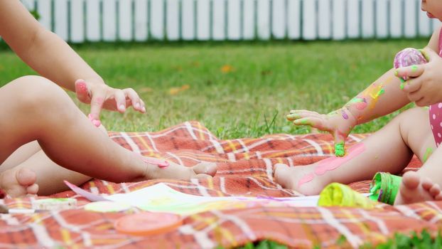 small children, a four-year-old boy and a one-year-old girl, brother and sister, play together, paint with finger paints, in the garden, sitting on a blanket, on grass, lawn, in summer. High quality photo