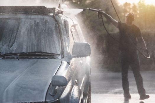 A man with a high pressure hose washes off the foam with water at a self-service car wash.