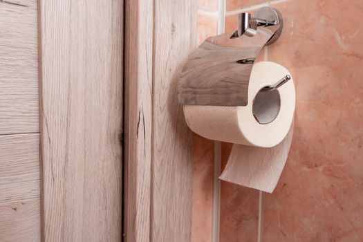 a roll of toilet paper hanging in a holder in the toilet. A roll of soft toilet paper hanging on a modern chrome holder on a toilet wall. High quality photo