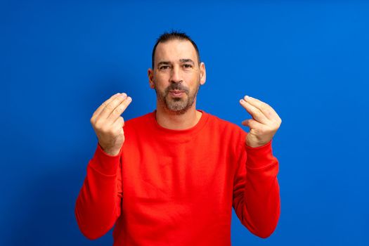 Latin man about 40s with beard wearing red jumper over isolated blue background doing italian gesture with hands and fingers confident expression