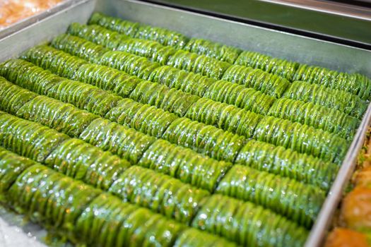 Close-up of green pistachio baklava on the counter among other types of baklava. Selective soft focus on turkish dessert.