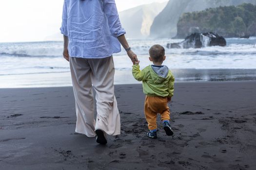 Mother and little child holding hands walking at sea side. High quality photo