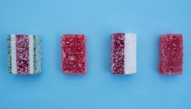 Four red gelatin candies on blue paper background. Flatlay of square red marmalade pieces.