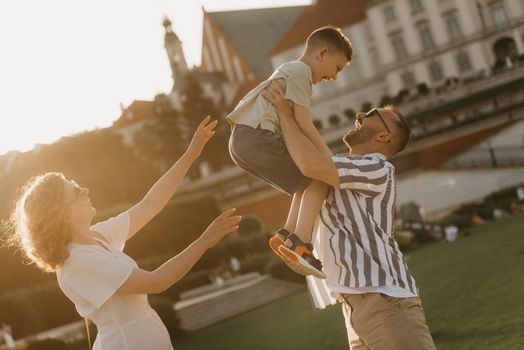 Father, mother, and son are having fun in an old European town. Happy family in the evening. Dad is throwing his little boy up near mom.
