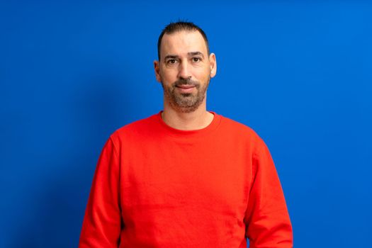 Spanish man with a beard posing happily for a half body portrait isolated on blue studio background