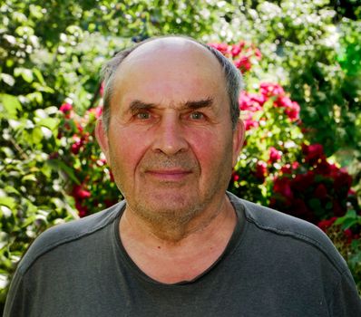 Signor in a T-shirt with a positive look on a blurred background of vegetation. A pensioner in the country.