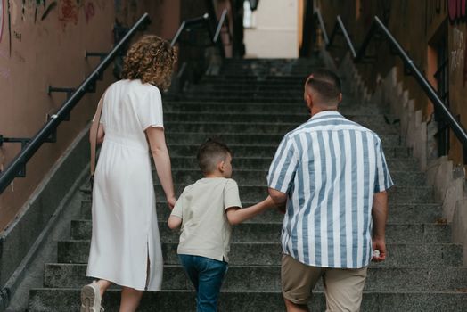 A photo from the back of a family which is climbing stairs in an old European town. A happy father, mother, and son are holding hands and having fun in the evening.