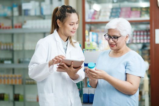 Young female pharmacist at the drugstore wearing white gown talking, giving advice, explaining, suggesting, and recommending to client or patient about the prescription and medications. Medicine and healthcare concept.