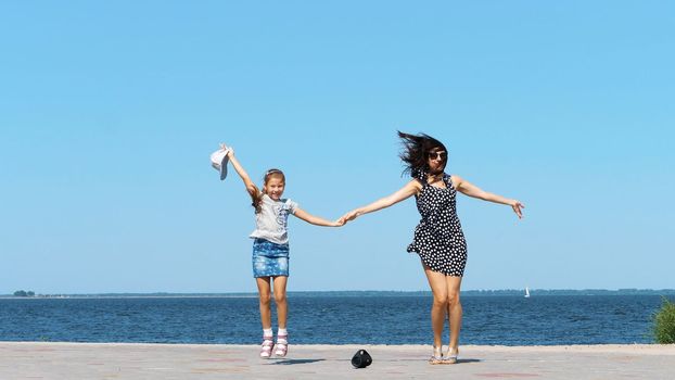 on beach mom and daughter, beautiful brunette in sundress and girl child teenager, dancing, listening to music with mini music bluetooth portable loudspeaker on a hot summer day. High quality photo