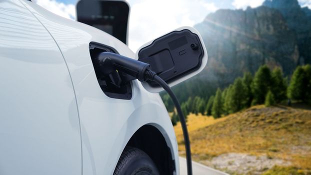 Energy sustainable car power by electro generator drive, recharge battery at charging station with mountain background for progressive travel concept. EV car in nature as symbol for clean environment.