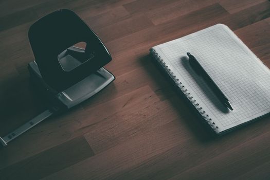 Notebook with pen near paper perforator on wooden table. Home office. Working from home