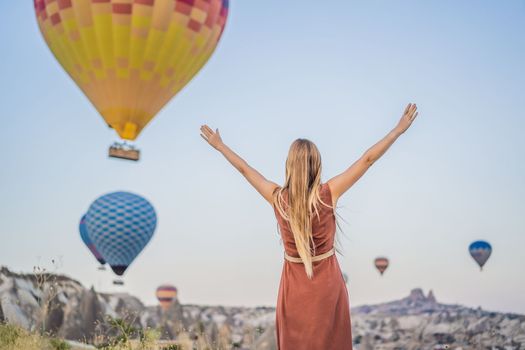 Tourist woman looking at hot air balloons in Cappadocia, Turkey. Happy Travel in Turkey concept. Woman on a mountain top enjoying wonderful view.