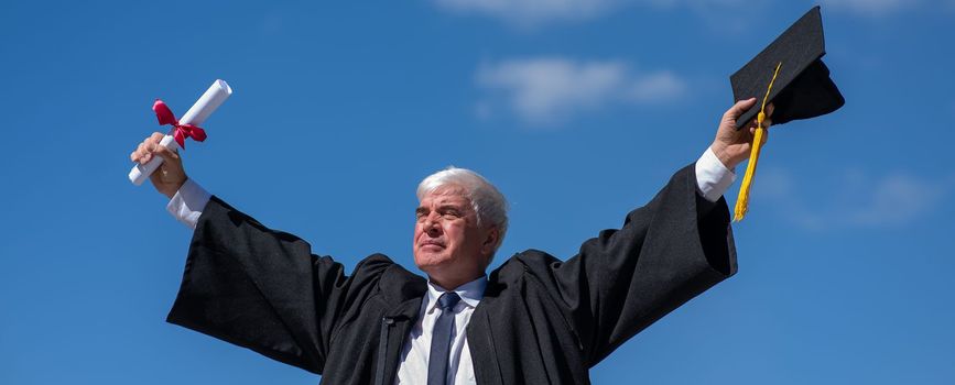 Elderly male graduate rejoices in receiving a diploma against a blue sky. Widescreen