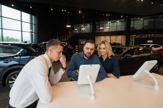 Caucasian married couple chooses a car in a car dealership on digital tablets