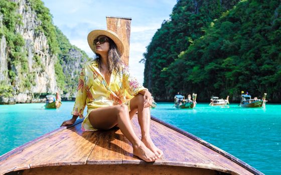 Asian women in front of a longtail boat at Kho Phi Phi Thailand, women in front of a boat at Pileh Lagoon with turqouse colored ocean