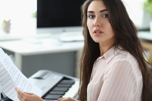 Woman holds musical notes and plays home synthesizer. Teaching music and musical notation concept