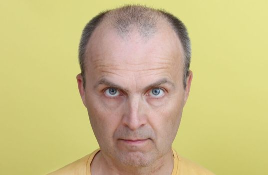 Handsome man after 40 years old in yellow T-shirt on yellow background looking at the camera.