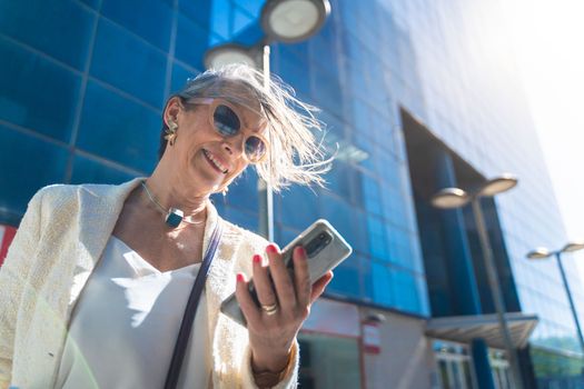 Attractive middle aged business woman looking at her smart phone in the street. High quality photo