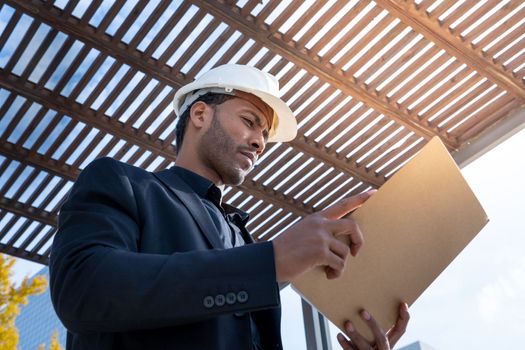 African American businessman manager with construction helmet reviewing blueprints for a building project. Business, finance and industry concept. High quality photo