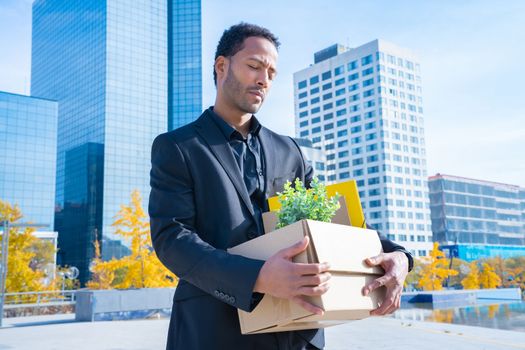 Businessman with cardboard box with office supplies standing outside office building. Fired concept. High quality photo