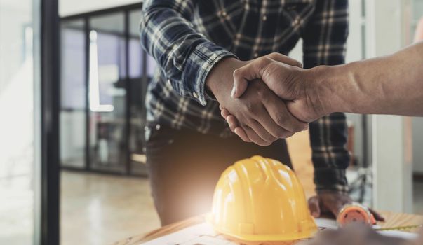 Engineers or architecture shaking hands at construction site for architectural project, holding safety helmet on their hands