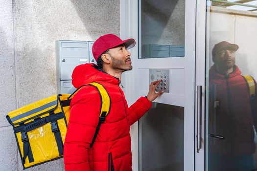 young African American food delivery worker in a doorway knocking at the doorbell of an apartment block. High quality photo