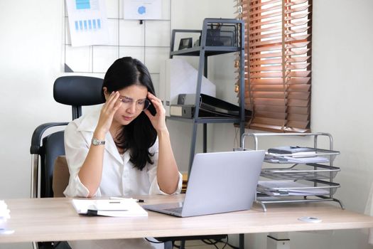 Tired female employee holding head on hand, looking at computer screen, doing hard task, having problem with computer software. Stressed exhausted businesswoman suffering from headache, feeling bored