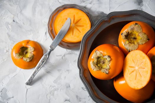 still life with persimmon on a gray cement background in a pewter dish, colorful flatley, healthy food,. High quality photo