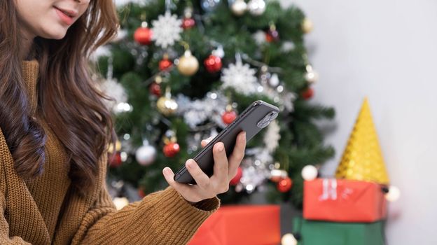 Close up overjoyed asian woman using phone, celebrating success, showing yes gesture, sitting on Christmas tree background at home, received great news, shopping sale, reading message..