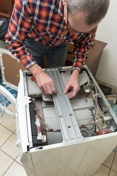 Middle aged man repairing broken washing machine with tools, household chores. High quality photo