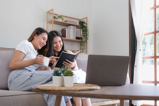 Two female friends reading book while another looking at her smiling playful.