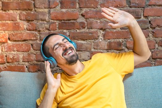 Portrait of young handsome man listening to music with headphones against brick wall - High quality photo