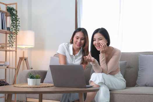 Two asian young woman happy smiling and using computer laptop on couch in living room at home..