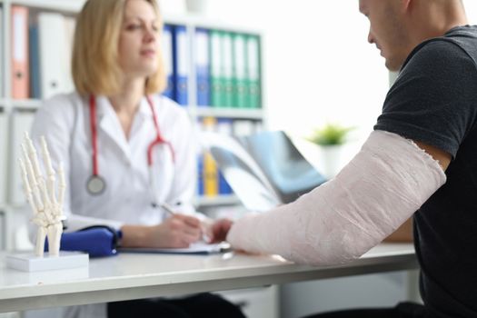Patient with plaster cast on broken arm consults doctor in hospital. Professional treatment of injuries and broken arm concept
