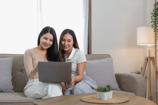 Two asian young woman happy smiling and using computer laptop on couch in living room at home..