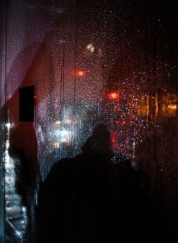 Blackout in Kyiv. Glass showcases with drops of rain and sleet on the streets of Kyiv illuminated by the headlights of cars and with silhouettes of people passing by