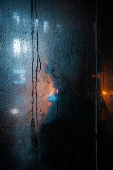 Blackout in Kyiv. Glass showcases with drops of rain and sleet on the streets of Kyiv illuminated by the headlights of cars and with silhouettes of people passing by