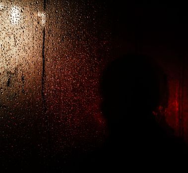 Blackout in Kyiv. Glass showcases with drops of rain and sleet on the streets of Kyiv illuminated by the headlights of cars and with silhouettes of people passing by