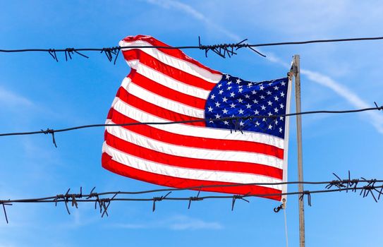 Barbed wire fence in front of Flag of United States of America waving in the wind with sky background